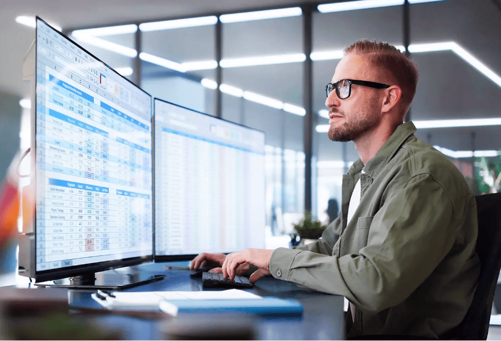 Elektroentwickler arbeitet konzentriert am Computer mit zwei großen Monitoren, analysiert technische Daten – sinnbildlich für eine Stelle in der Entwicklung analoger und digitaler Schaltungen für Batteriesysteme.
