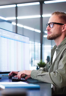 Elektroentwickler arbeitet konzentriert am Computer mit zwei großen Monitoren, analysiert technische Daten – sinnbildlich für eine Stelle in der Entwicklung analoger und digitaler Schaltungen für Batteriesysteme.
