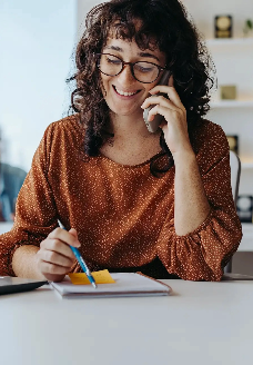 Projektmanagerin im Gespräch am Telefon in einem modernen Büro, arbeitet mit Laptop und Notizblock – symbolisch für eine Stelle im Projektmanagement für innovative Batteriesysteme.