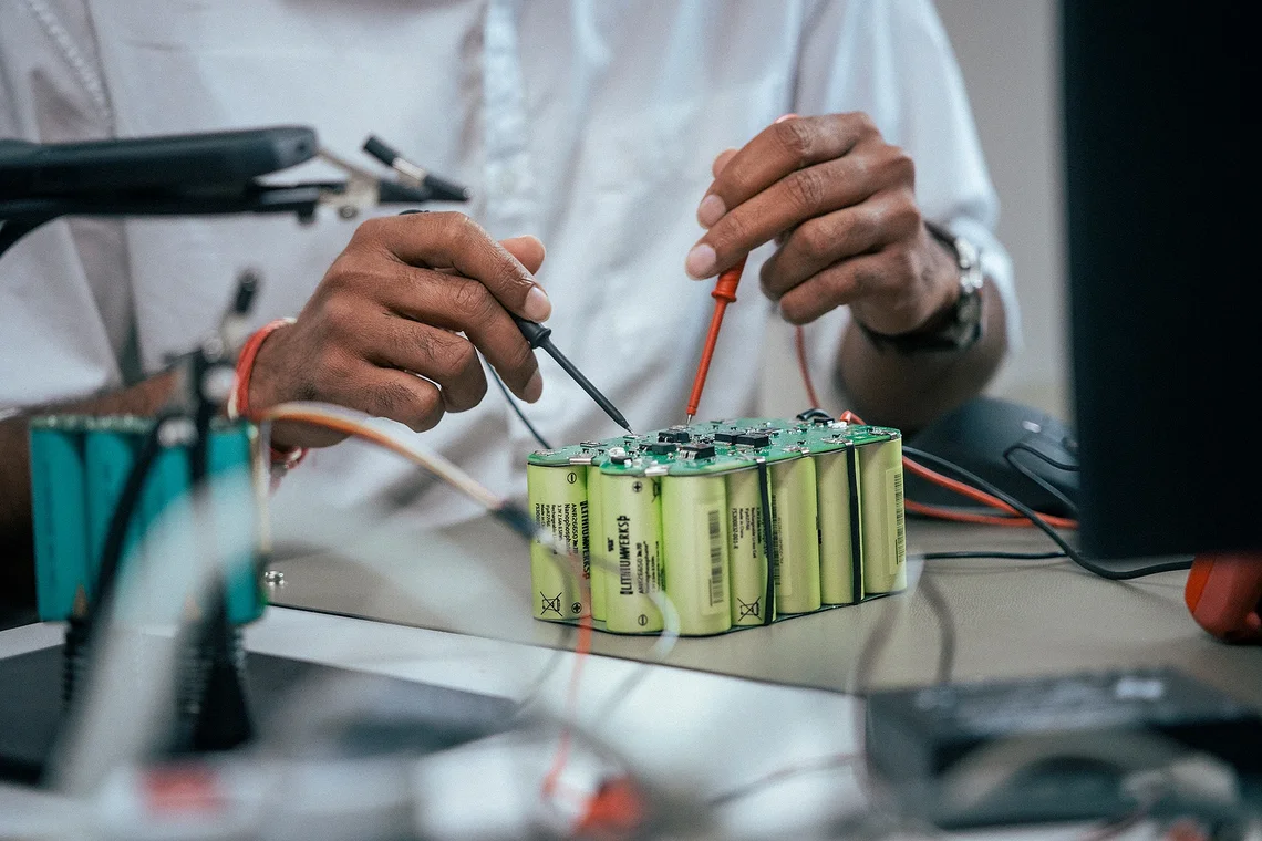 Techniker misst mit Prüfspitzen an einem Batteriemodul aus zylindrischen Zellen auf einem Labortisch.